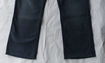 A pair of dark straight-leg jeans laid flat on pale paper, photographed from above